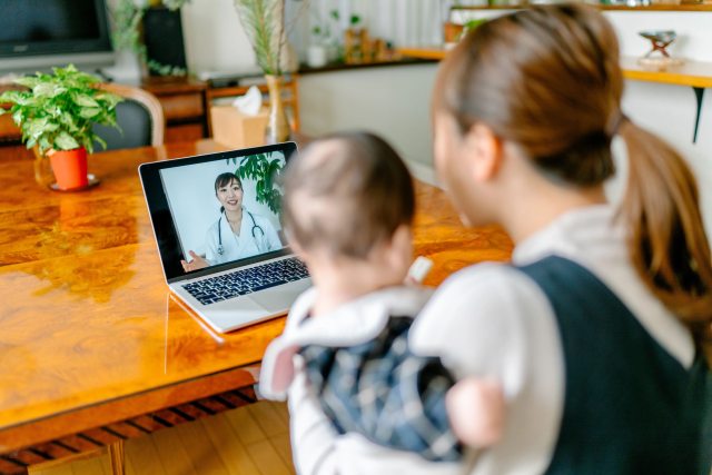 A woman holds her baby while talking to a doctor via a telehealth appointment.