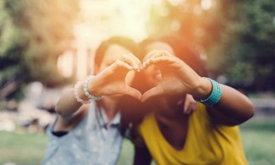Two young women in a back yard facing the camera and holding their hands up to form a heart with their fingers.