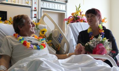 A couple in a hospital room, one a patient, with leis around their necks  in discussion