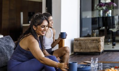 2 women with light brown skin relax on a couch with beverages