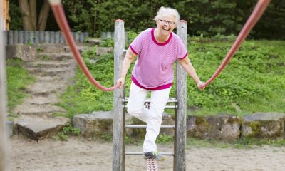 Smiling woman with short white hair balances on a piece of outdoor playground equipment
