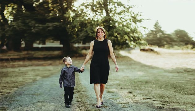 MaryAnn and child walk along a gravel road in a nature-filled area.