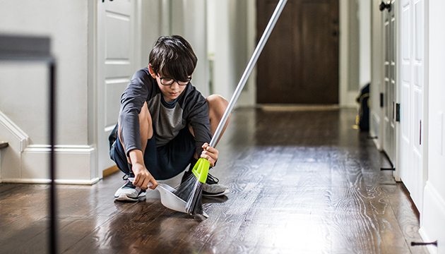 Young person in glasses uses broom and dustpan