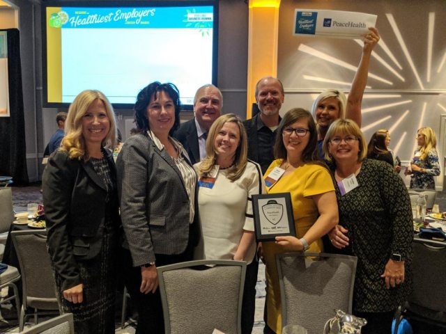 A group of eight PeaceHealth employees smiling and holding an award at a Healthiest Employer event