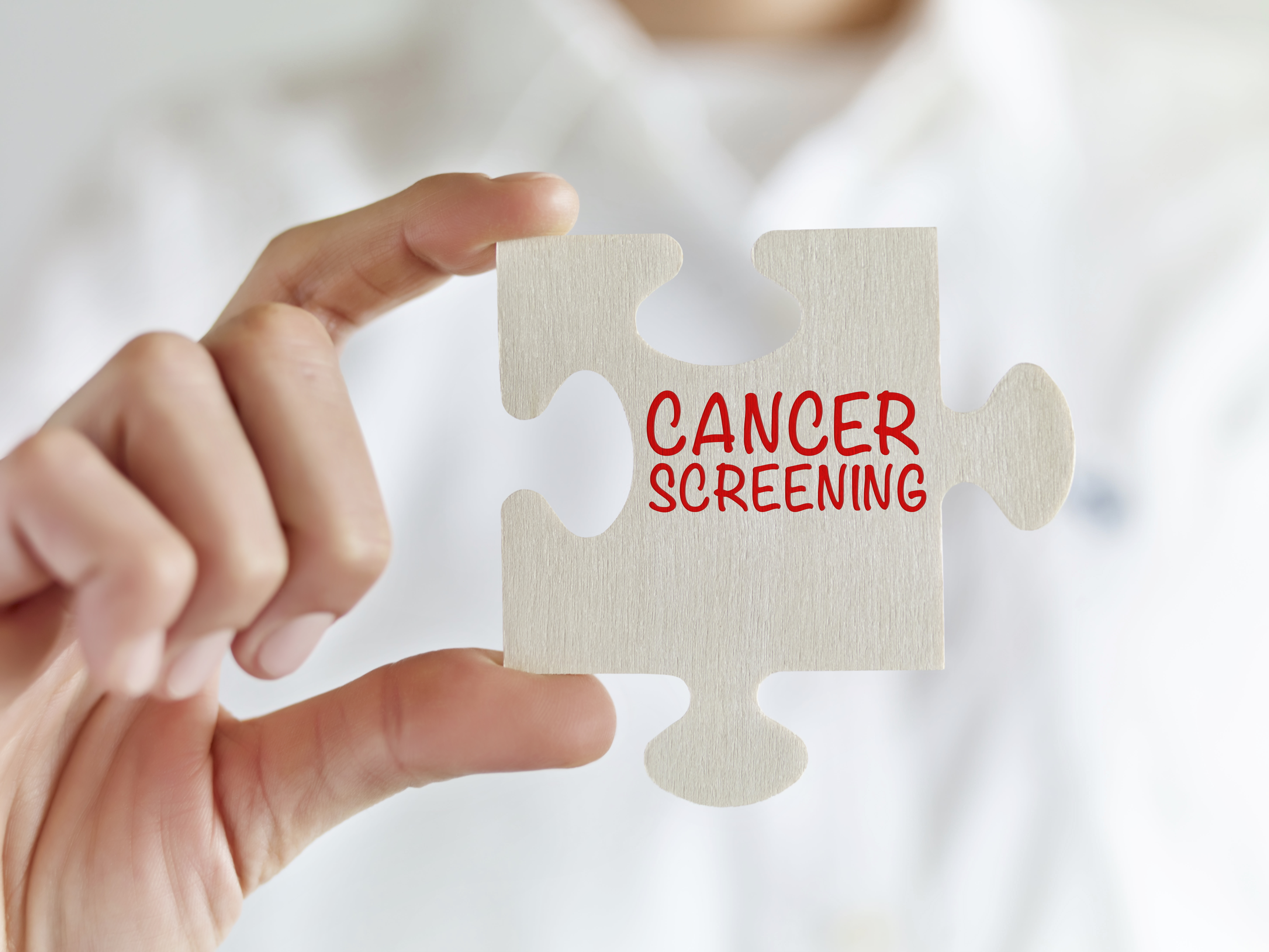 Person holding a white puzzle piece printed with the words "Cancer Screening" 