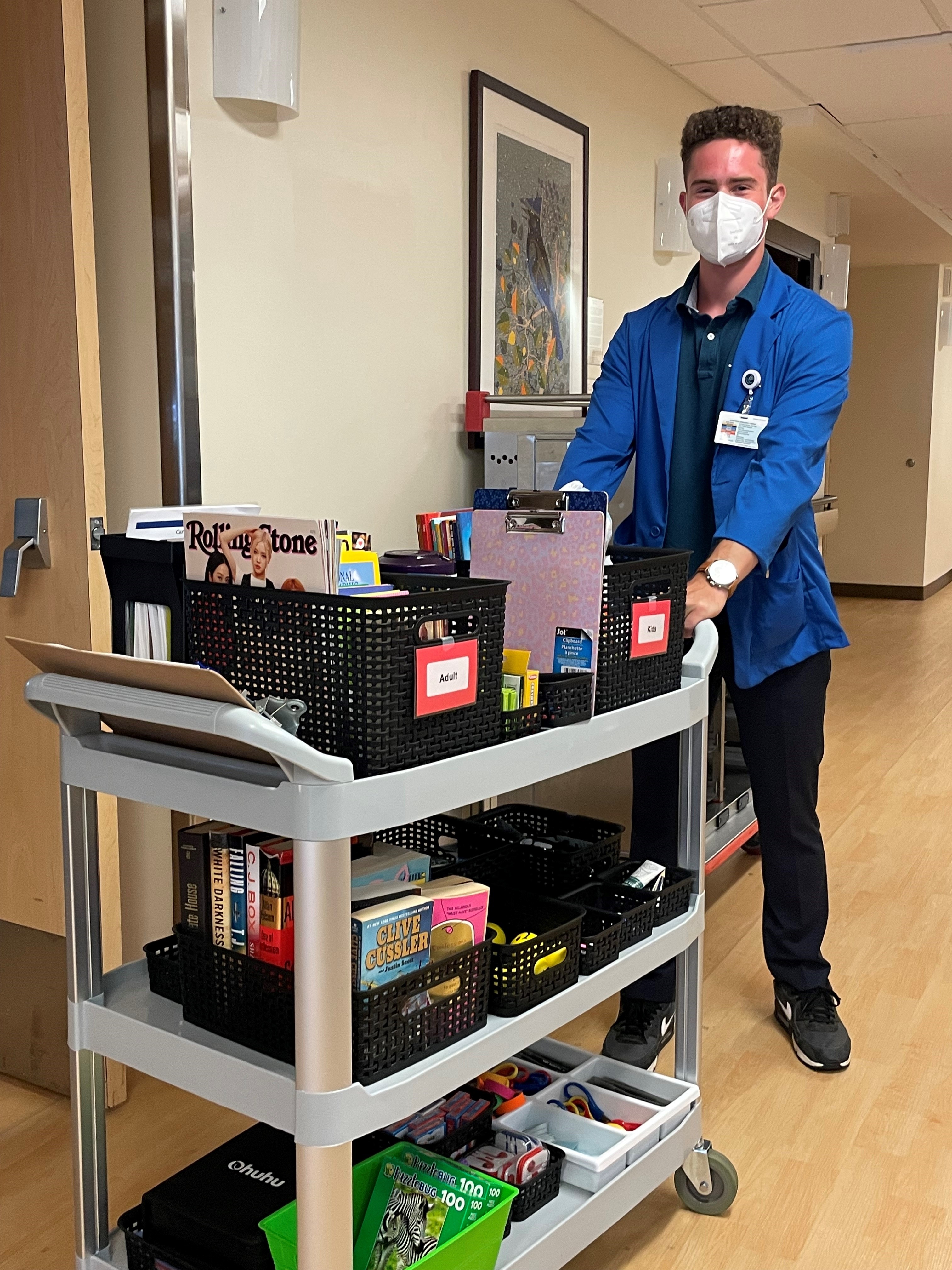 Young person pushing a cart of activity items in hospital hallway