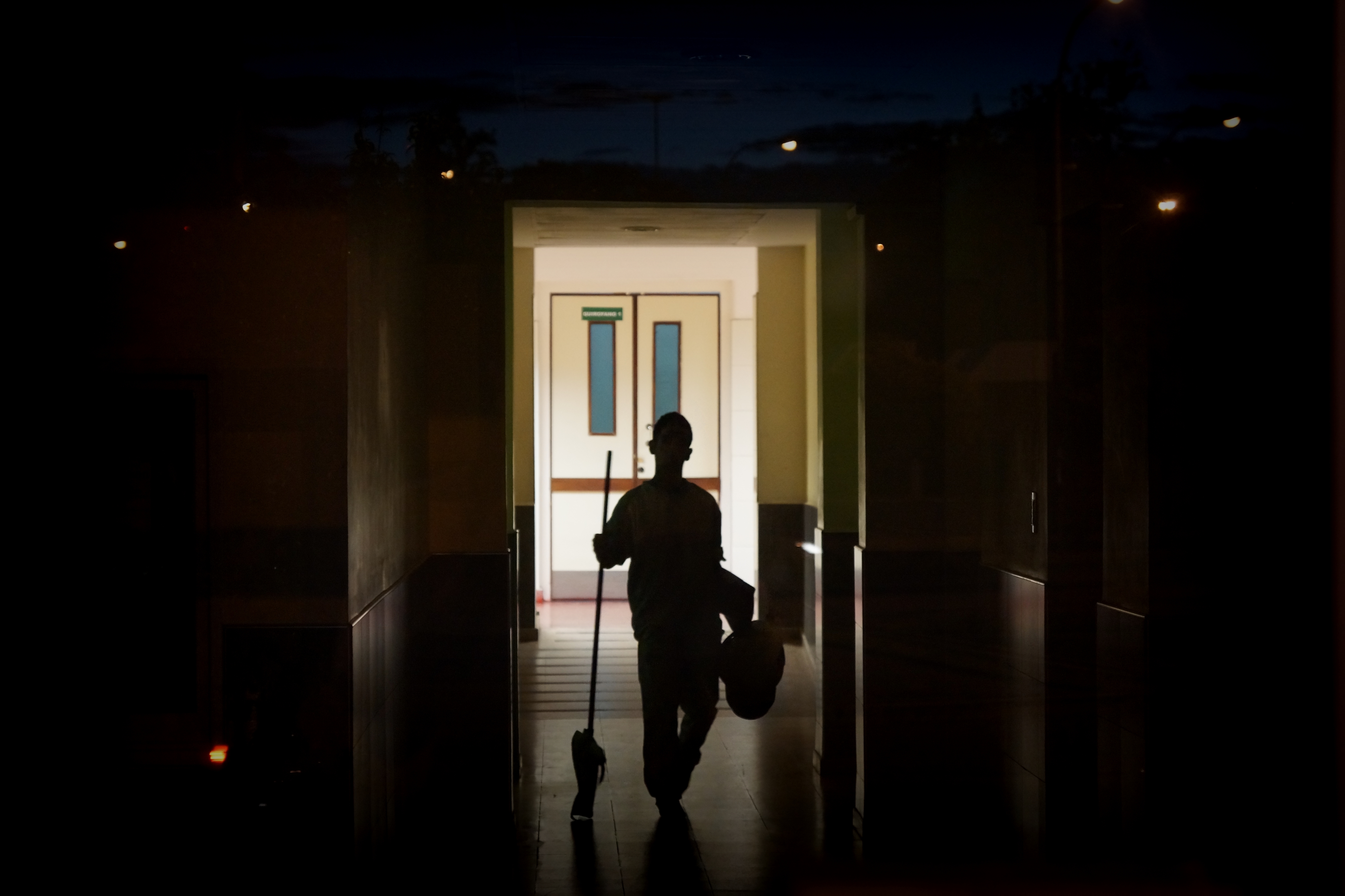 Worker holding a mop walks down a dark hallway