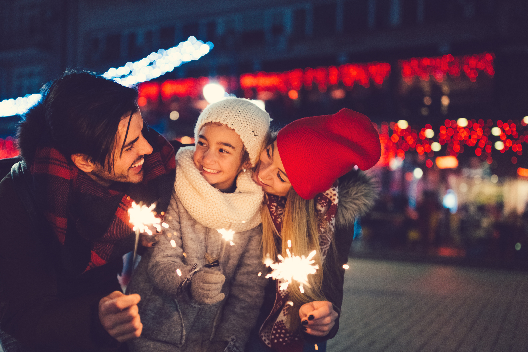 Two adults and young child hold sparklers to celebrate winter holiday