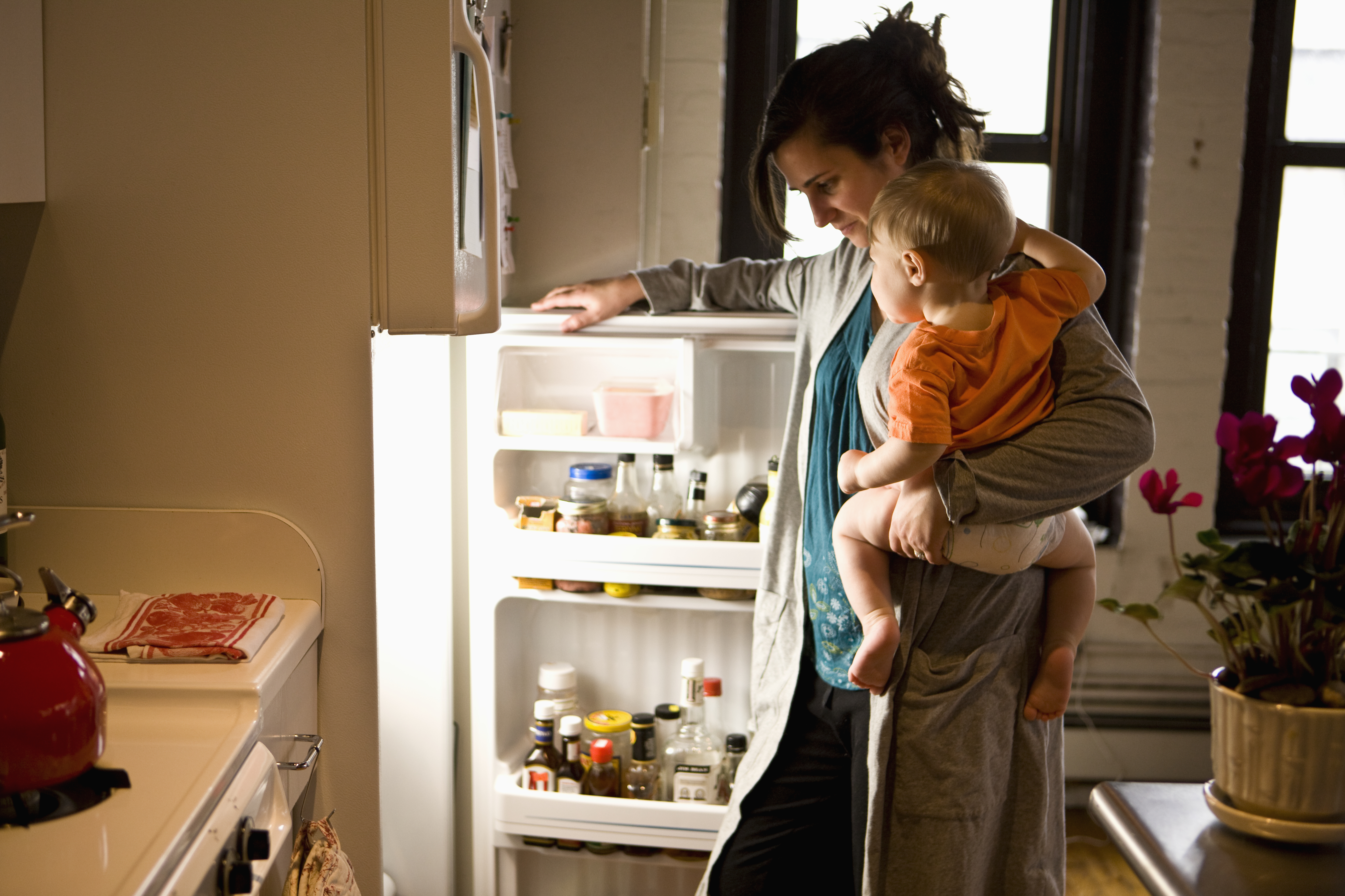 Woman looking in fridge with child on hip.