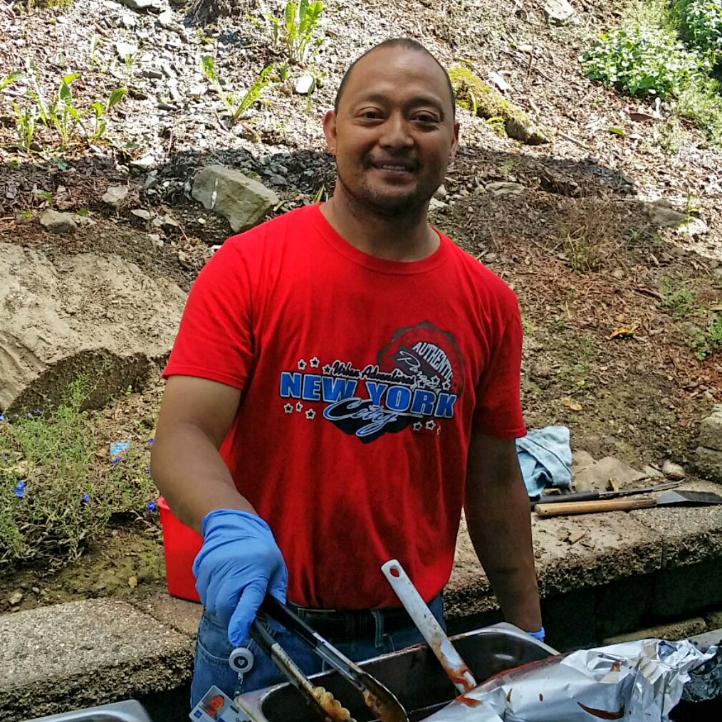 A man in a red shirt, serving dinner outside, stops to smile for a photo