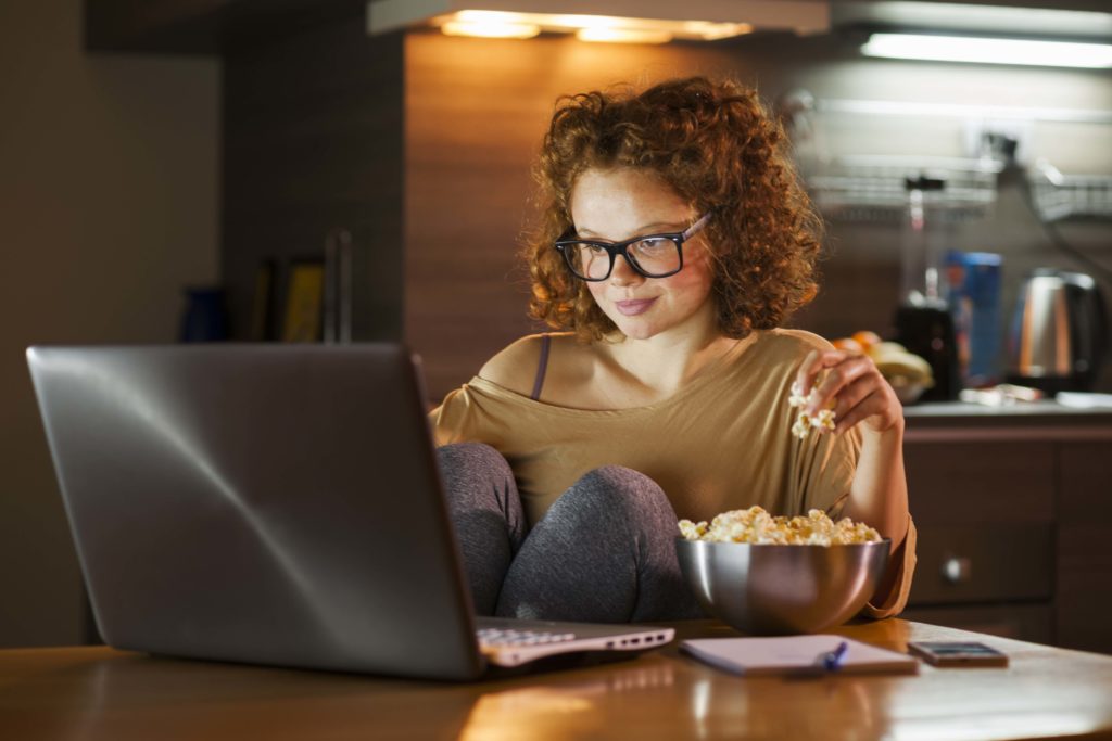 A young lady sits at her laptop with popcorn at her side