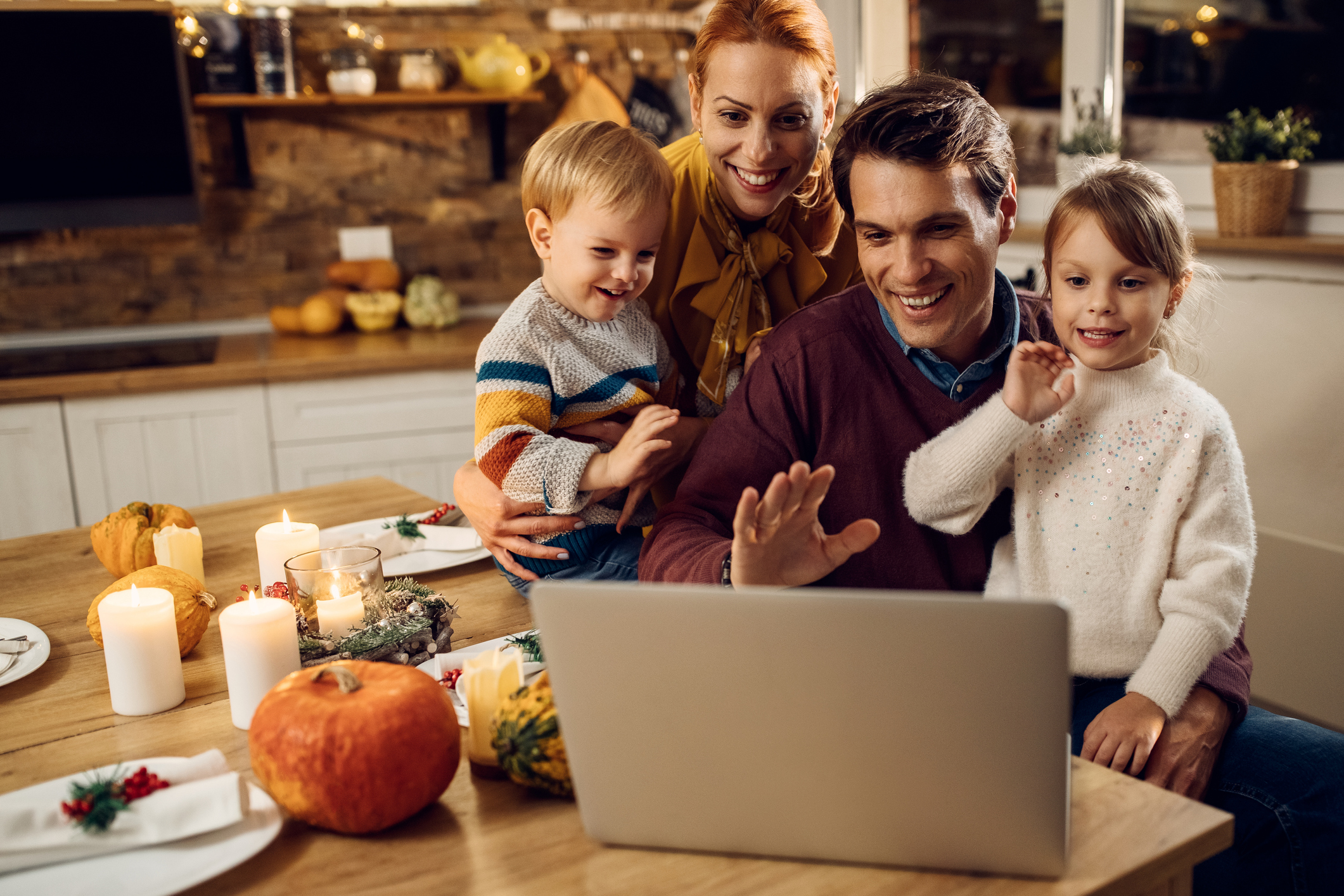 A family in their kitchen in front of a laptop, virtually meeting with others.