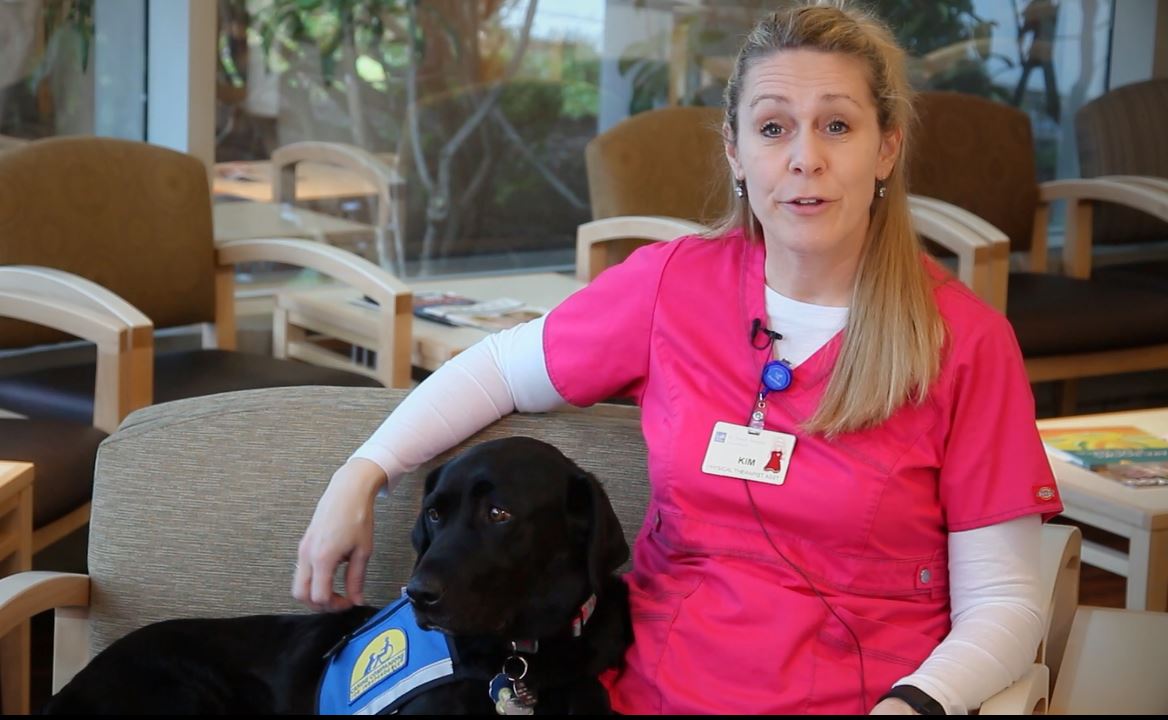 A provider speaks while petting a black labrador therapy dog