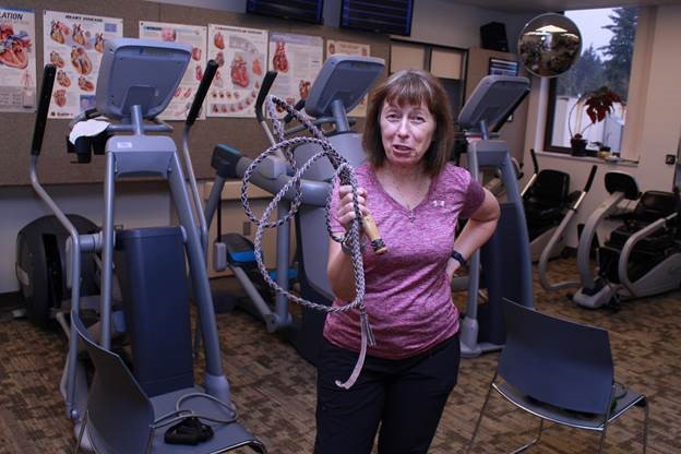 A woman holds cords in a room of exercise equipment