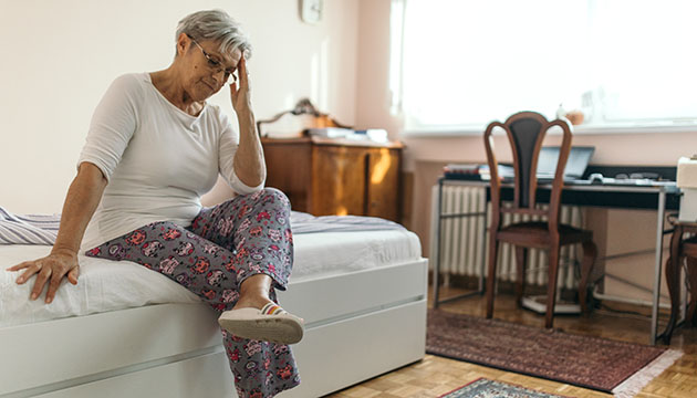 Older woman sitting on bed in possible pain