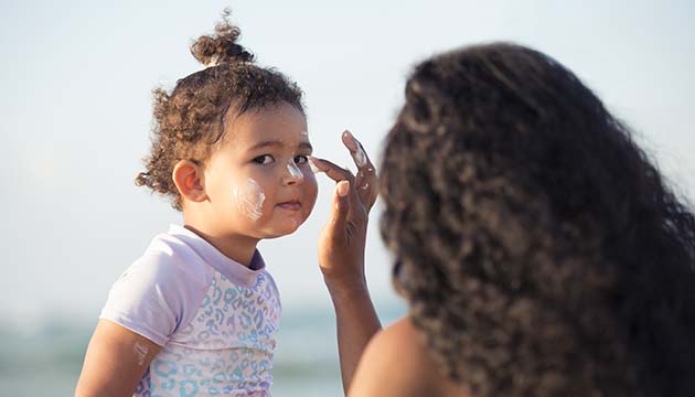 mom applies sunscreen to a toddler at the beach