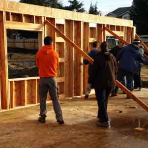 A group of volunteers hoist a beam of wood up to support construction of a new house wall.
