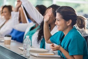 A smiling medical student raises their hand in a classroom setting.