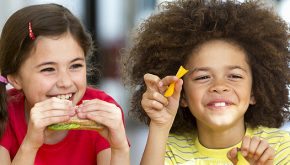 Two children laugh and eat lunch 