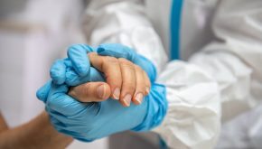 A provider with gloves holds the hands of a patient