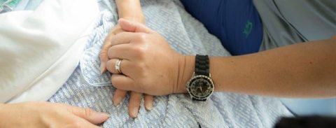Tight cropped photo of a caregiver or family member holding the hand of a patient in a comforting manner.