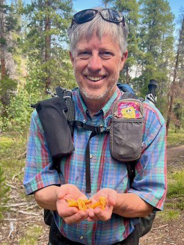 Smiling man holds hands full of mushrooms on a trail outside