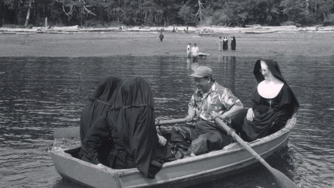 Nuns ride in a boat near the shore while another person rows.