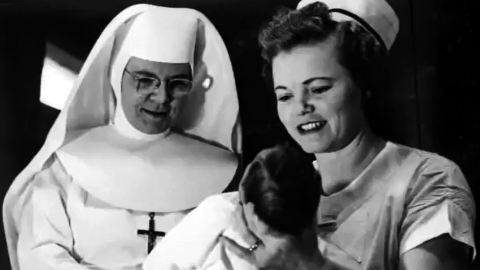 A nurse holds a baby as a sister looks on smiling