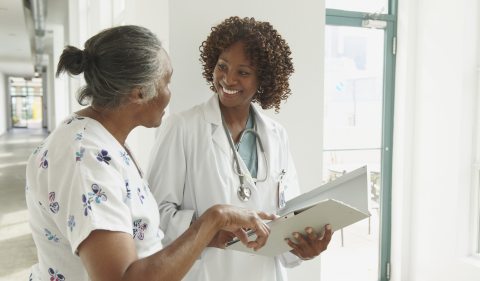A healthcare provider speaks to an older person in a patient gown