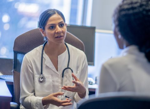 A female doctor speaking to a female patient in a clinical setting while gesturing with hands