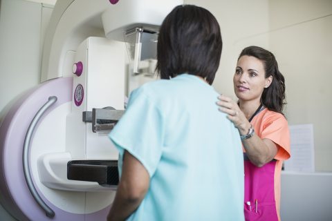 A healthcare provider helps a patient step up to the mammogram machine