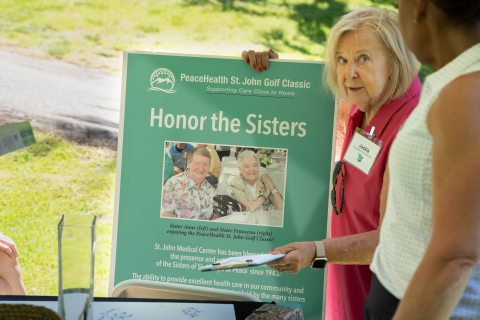 A volunteer at the peacehealth st. john golf classic showing a sign that says "honor the sisters"