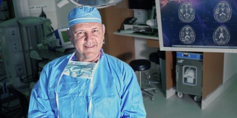 Neurology doctor smiling at the camera and next to brain scans