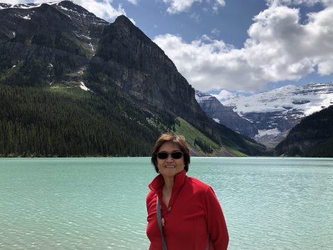 Cynthia standing in front of a lake and mountain range smiling at the camera