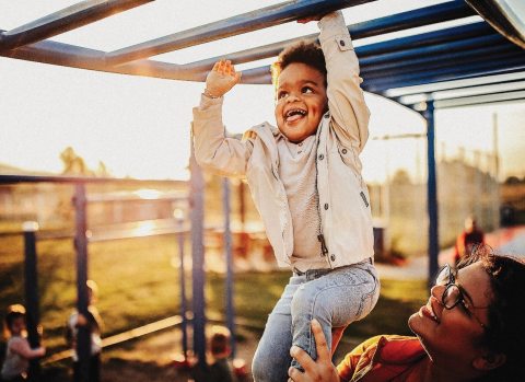 Child playing on monkey bars while woman supports him from below