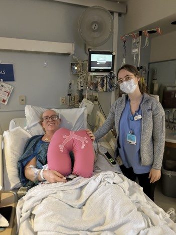 Bret in a hospital bed holding a stuffed plushie of pair of lungs with a caregiver