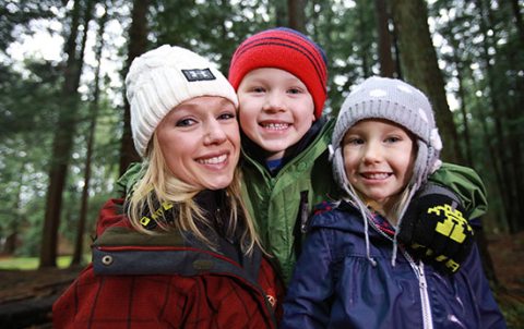 A mother and her two children smile while looking at the camera in a park-like setting