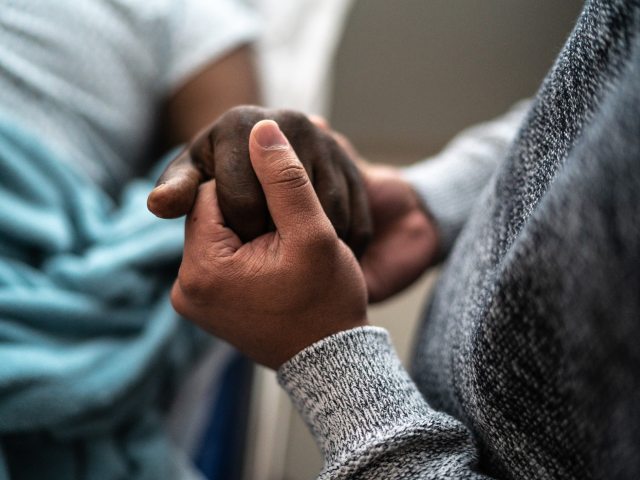 A father holds the hand of his son in a comforting manner.