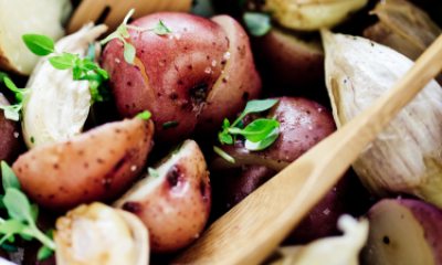 A wooden sppon rests in a red potato salad with herbs and garlic 