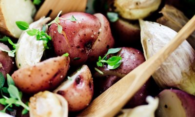 A wooden sppon rests in a red potato salad with herbs and garlic 