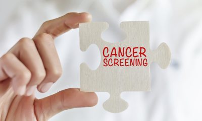 Person holding a white puzzle piece printed with the words "Cancer Screening" 