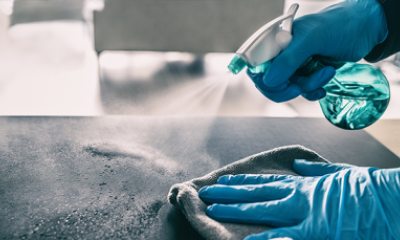 Gloved hands spray and wipe a surface