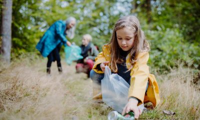 Young girl in a yellow rain jacket picks up litter from the ground.