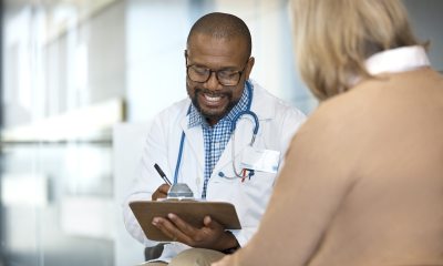 Black doctor writes on a clipboard while talking to a white woman