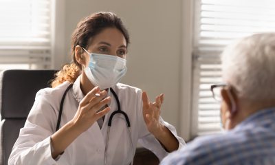 Close up of a female doctor wearing a face mask consulting with an older adult male patient  in doctor's office
