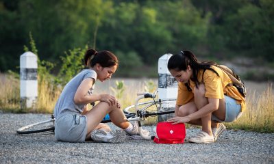 Young woman gives first aid to another woman sitting next to bicycle