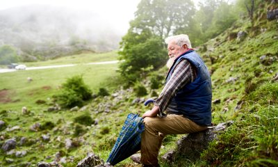 White-haired man sits on a rock on a hillside