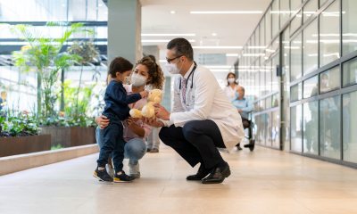 A young child and mother squat next to a doctor in a healthcare facility