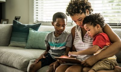 A woman sits on the couch with two children, working a tablet