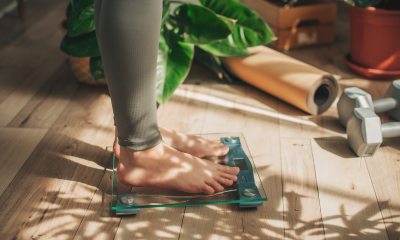 Feet of person standing on a scale next to yoga mat and weight set